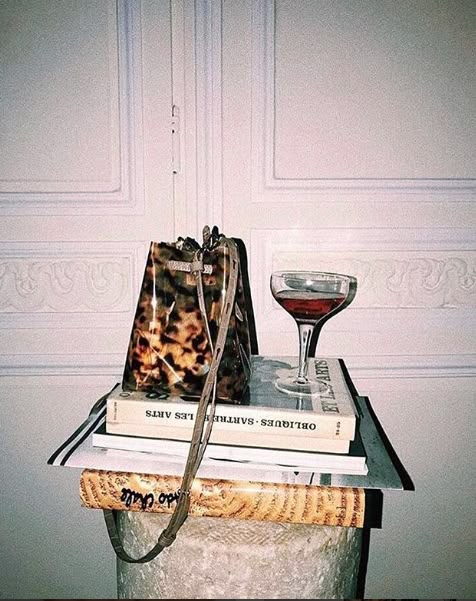Composición editorial con libros, copa y objetos sobre una mesa frente a una pared con molduras
