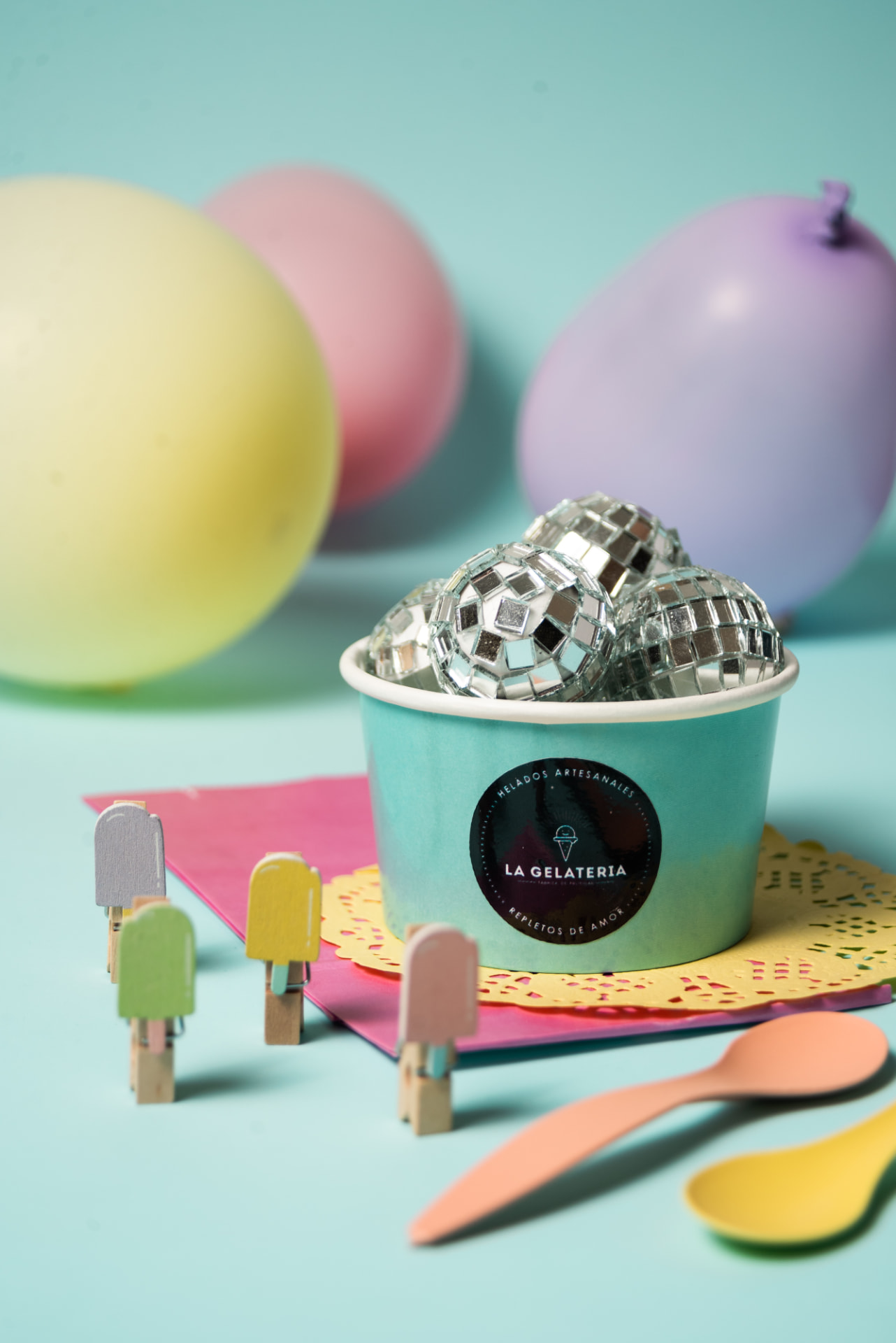 Pote turquesa de La Gelateria con bolas de espejos, globos pastel, broches con forma de helado y cucharitas de colores