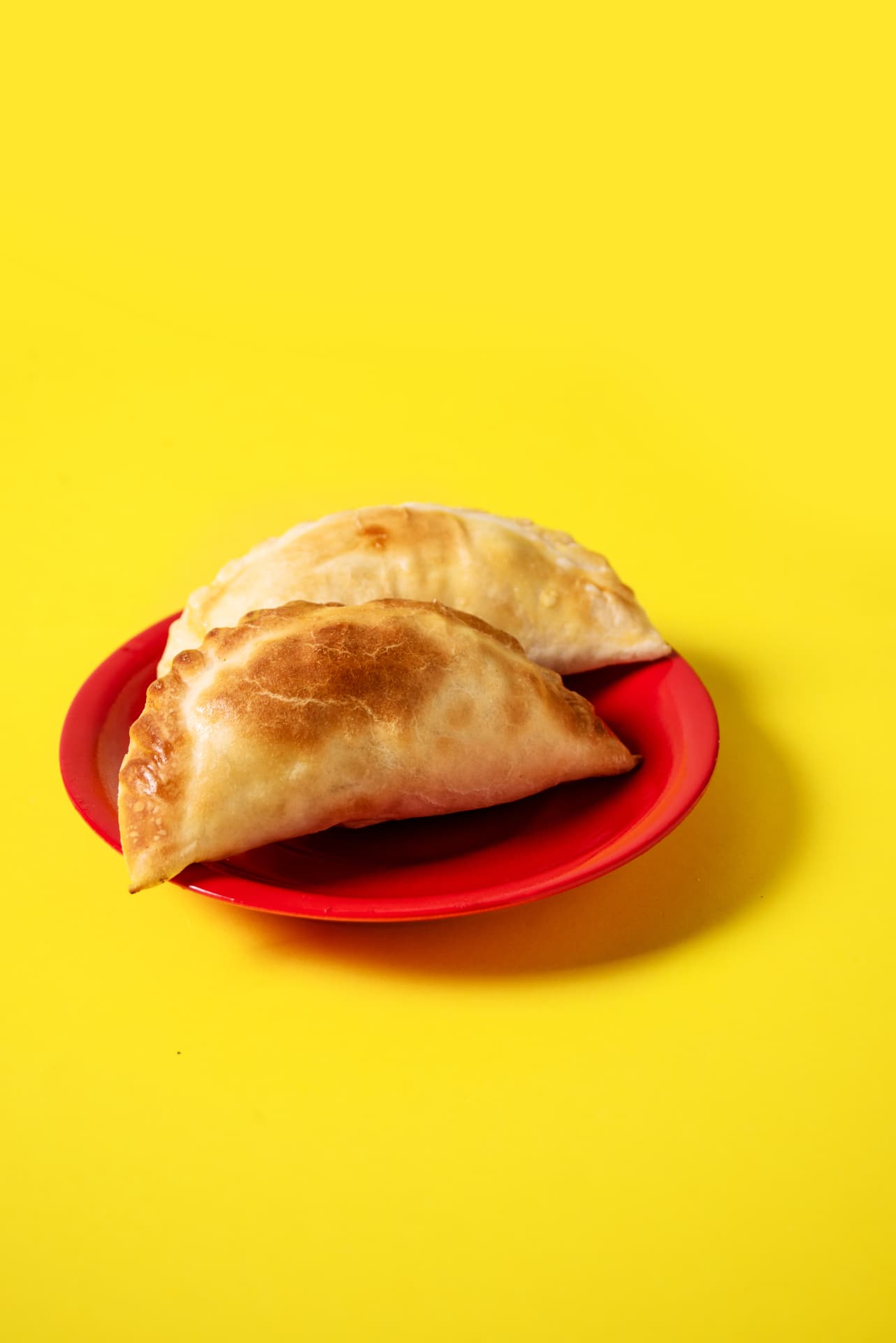 Primer plano de empanadas sobre plato rojo y fondo amarillo