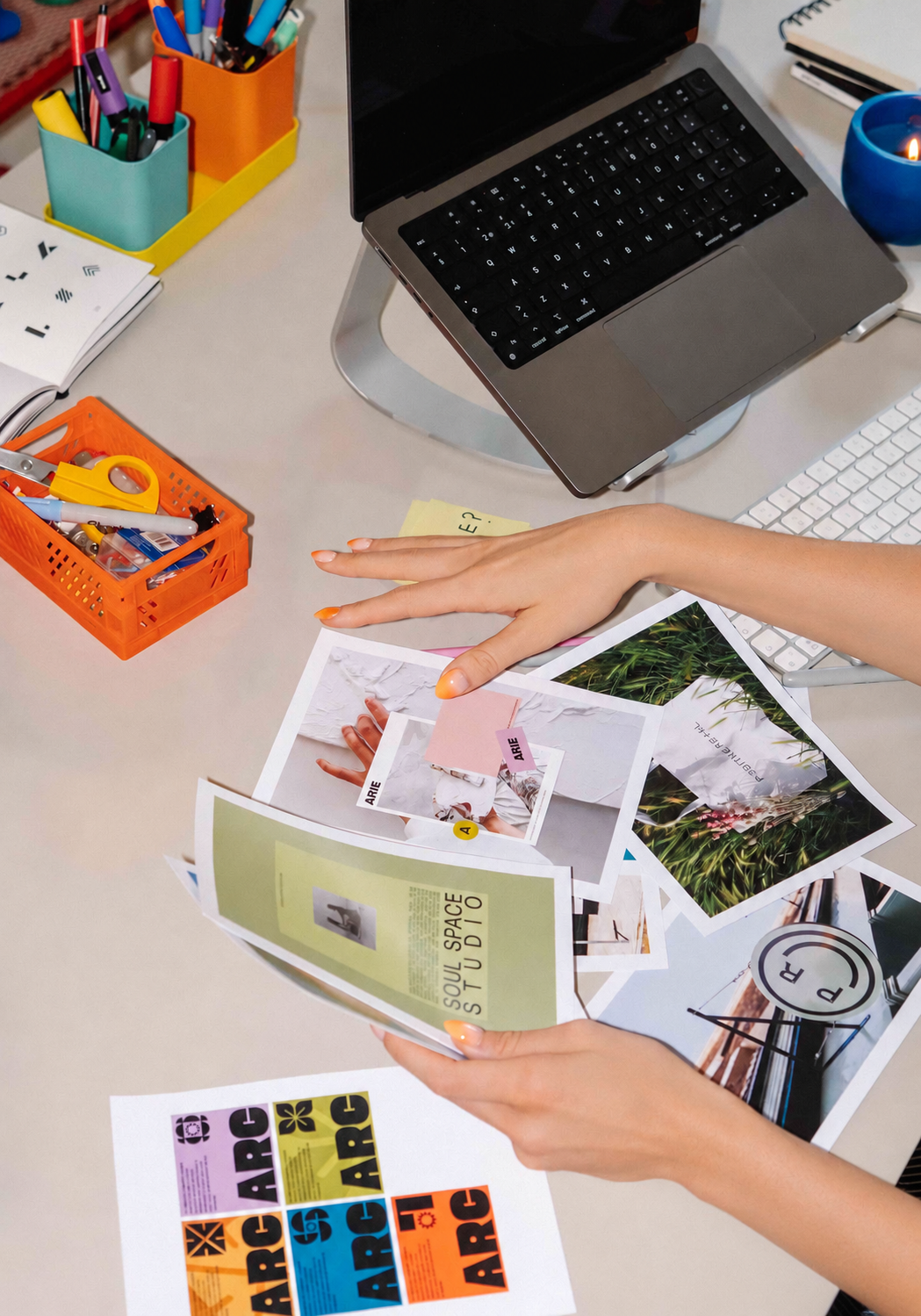 Mesa de trabajo con computadora, materiales de diseño, referencias gráficas y papeles impresos durante el desarrollo de una marca