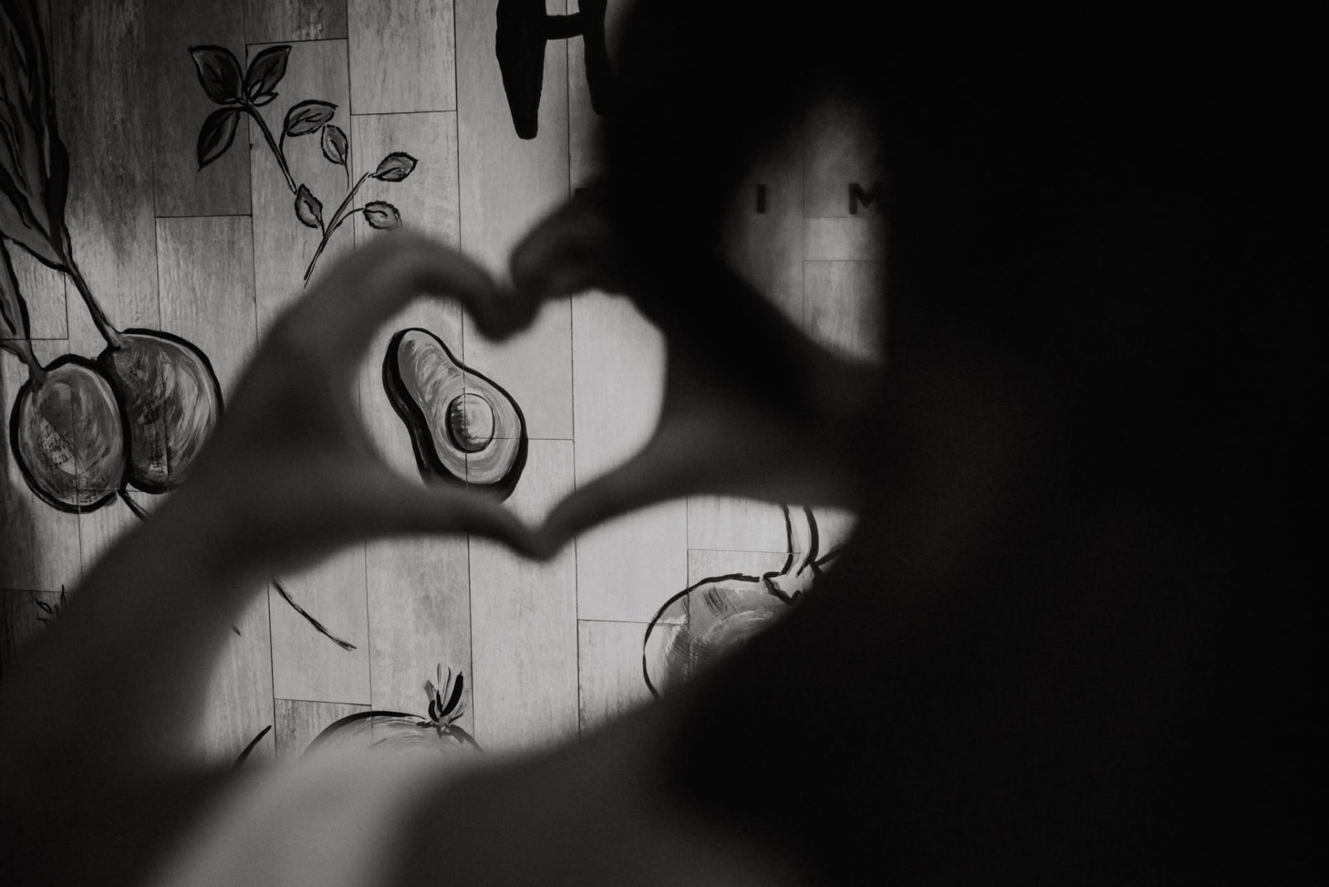 Manos formando un corazón frente al mural de Hipólito, fotografía en blanco y negro, 2020
